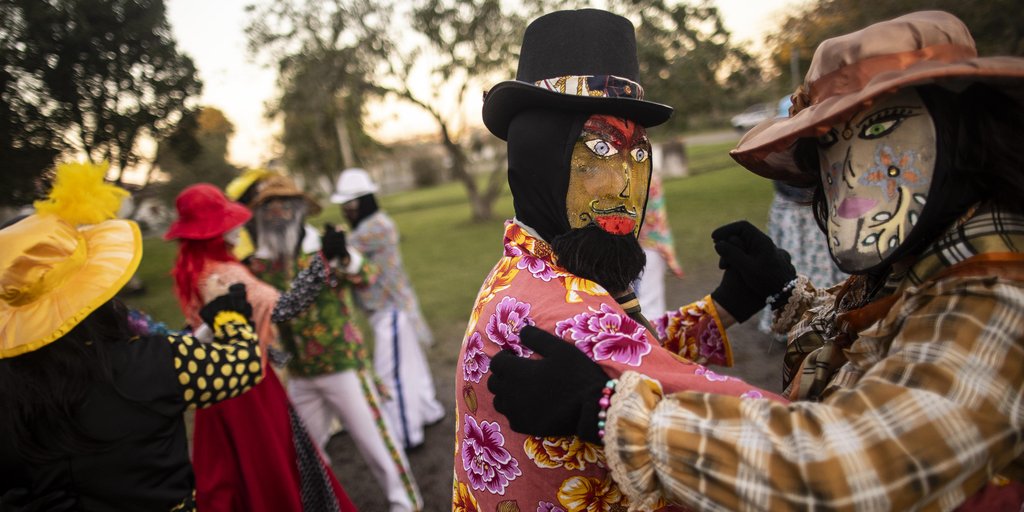Integrantes do Baile de Masquê com máscaras, vestidos coloridos e chapéus