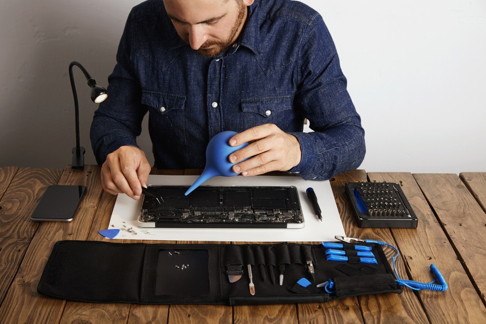 Pessoa limpa teclado de notebook com ferramentas de manutenção