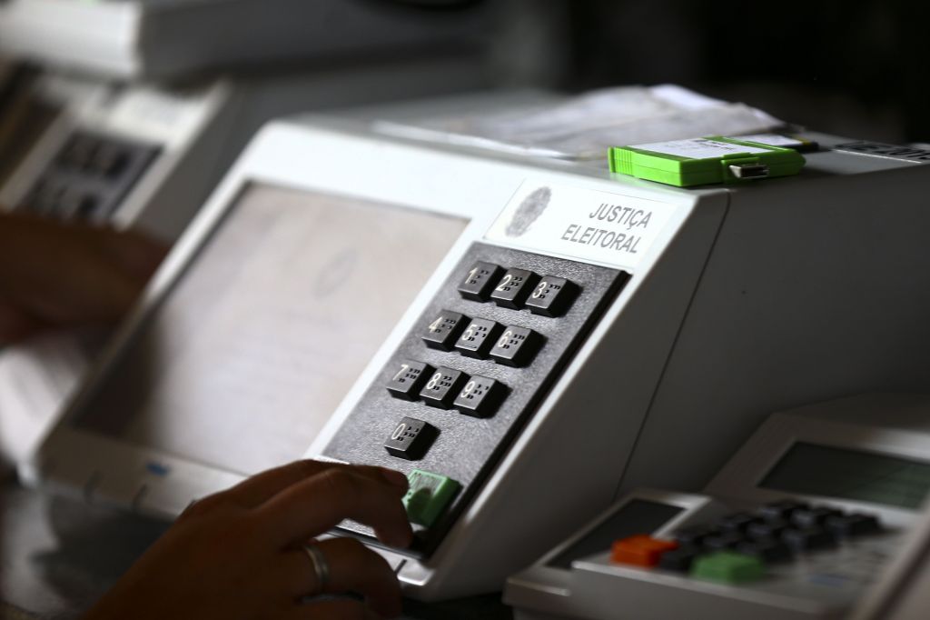 Mão pressiona o botão Confirma de urna eletrônica
