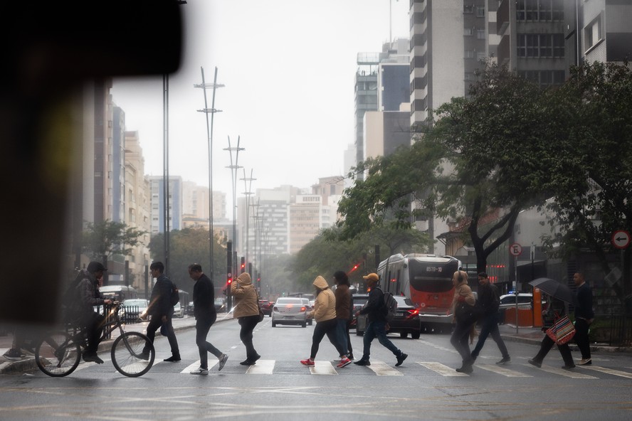 Pedestres atravessam a Avenida Paulista sob frio e chuva em São Paulo