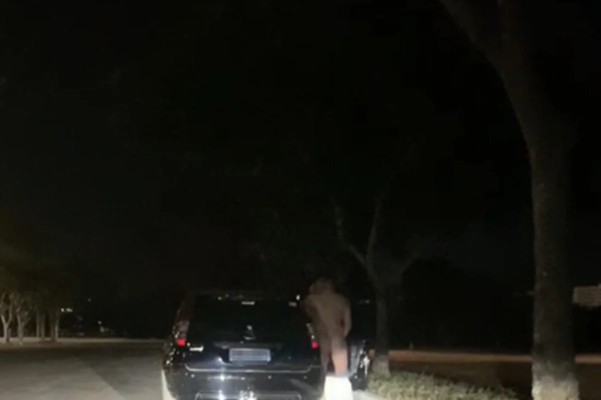 Homem sem roupas ao lado de veículo em estacionamento