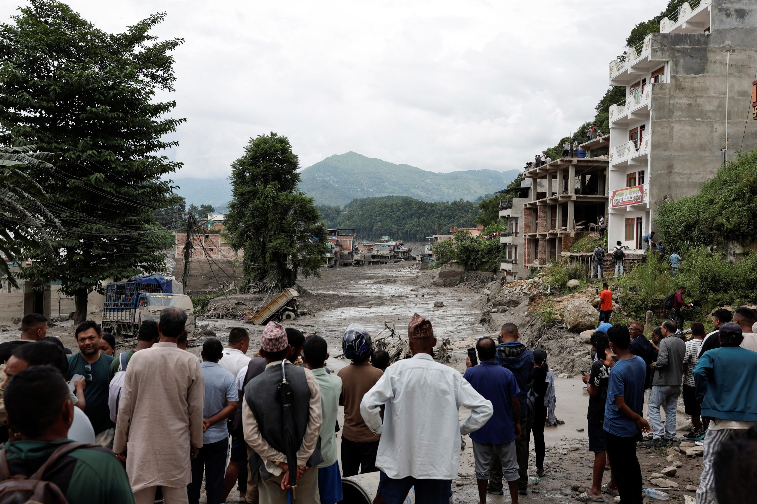 Pessoas perto de casas e estrada cobertas por lama em Trishuli, no Nepal