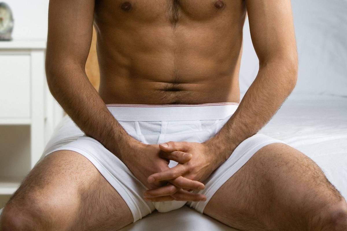 Homem de cueca branca sentado na beira de uma cama