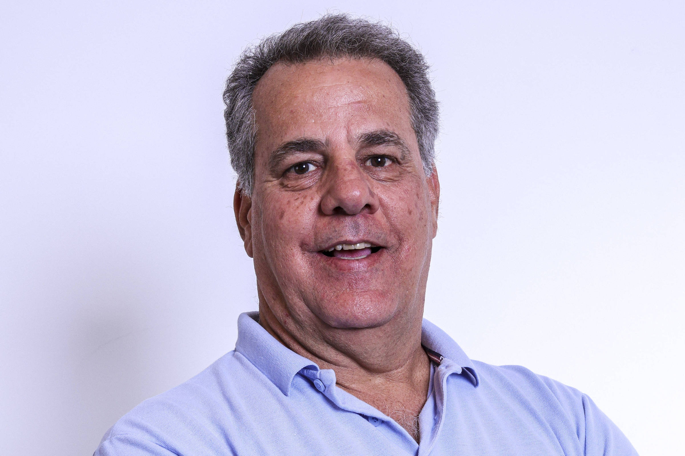 Pedro Suplicy com camisa polo azul-clara e braços cruzados diante de fundo branco