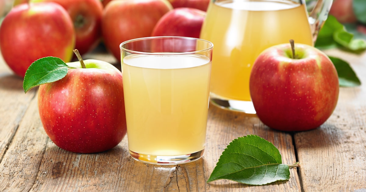 Copo e jarra com suco de maçã ao lado de maçãs fatiadas