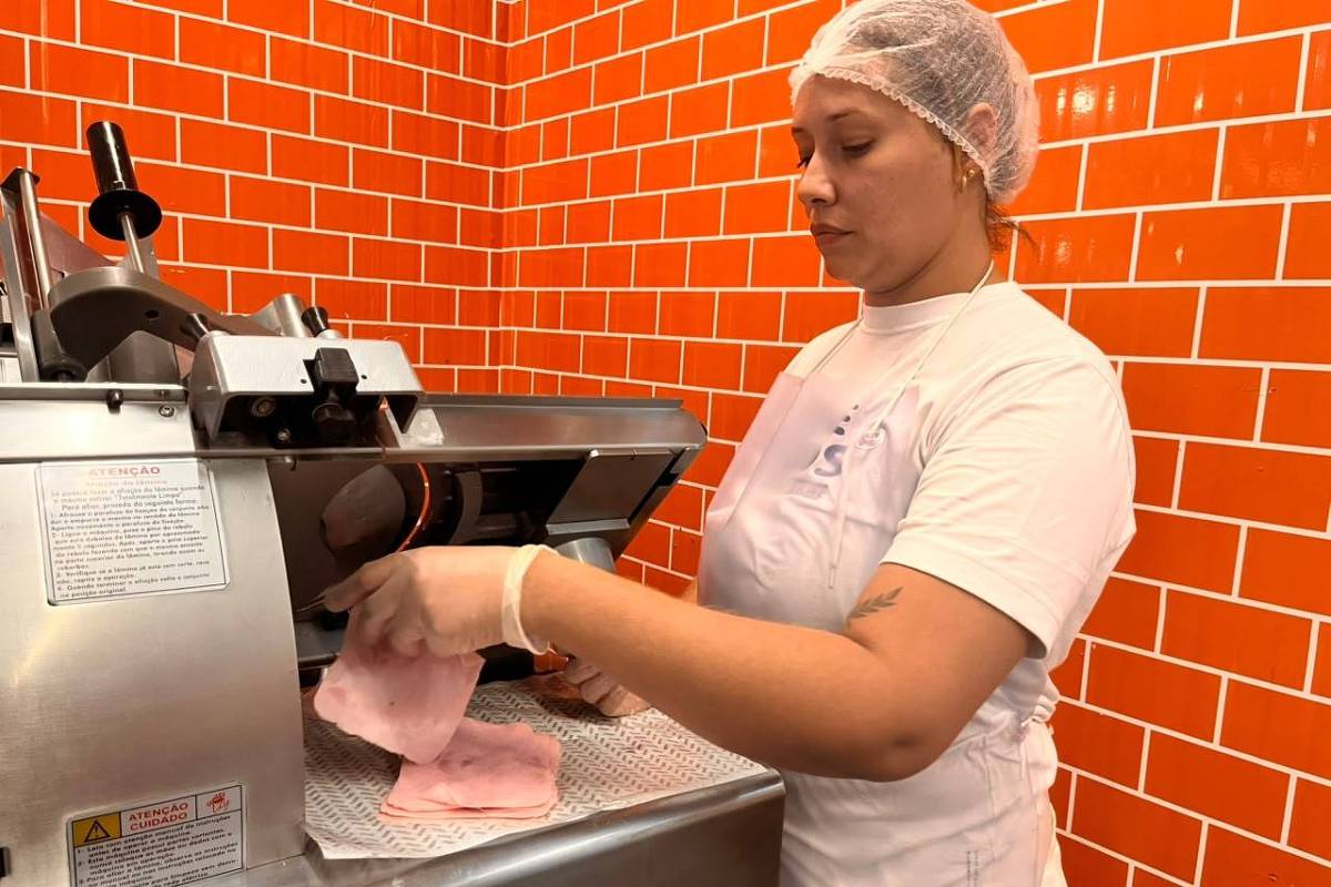 Atendente de frios corta carne em fatiadora industrial