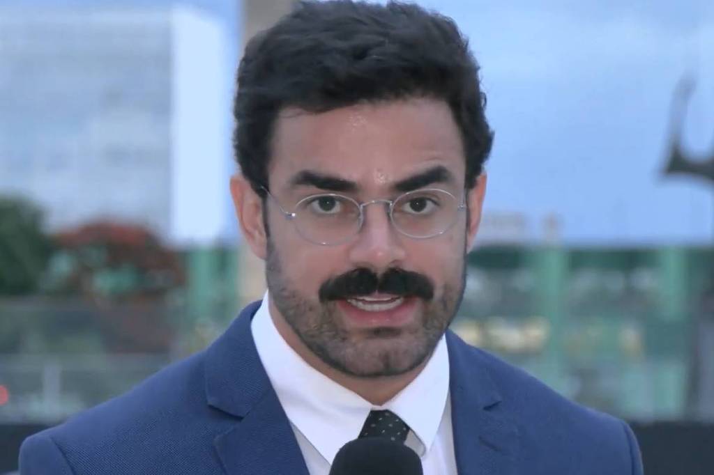 Túlio Amâncio fala ao microfone usando terno azul