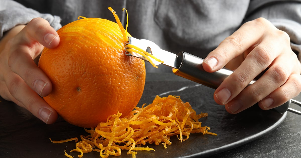 Mãos raspam casca de laranja sobre um prato