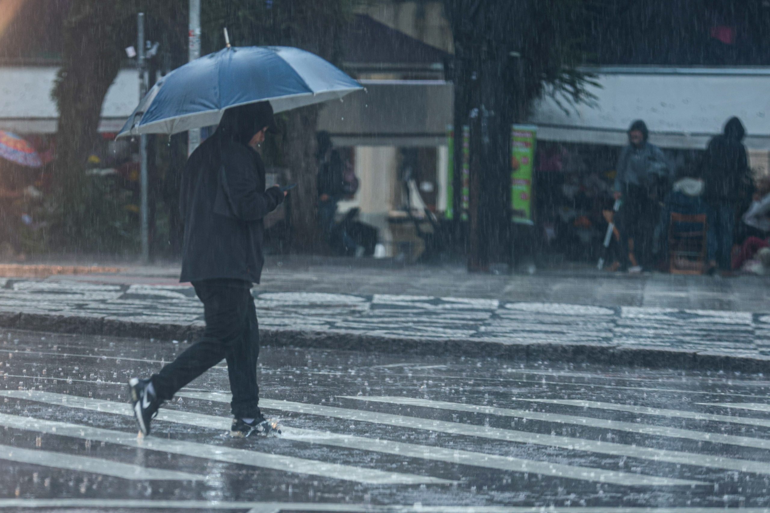 Pessoa caminha com guarda-chuva durante chuva em Curitiba