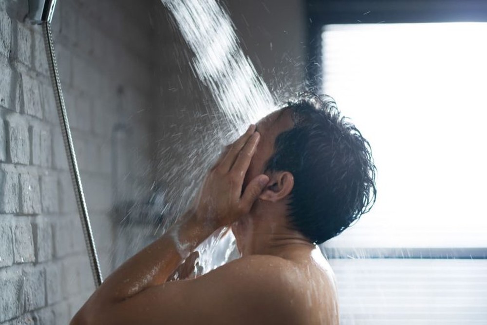 Pessoa limpa os furos de um chuveiro com as pontas dos dedos