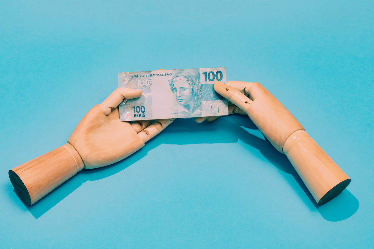 Mãos seguram uma cédula de 100 reais sobre fundo azul