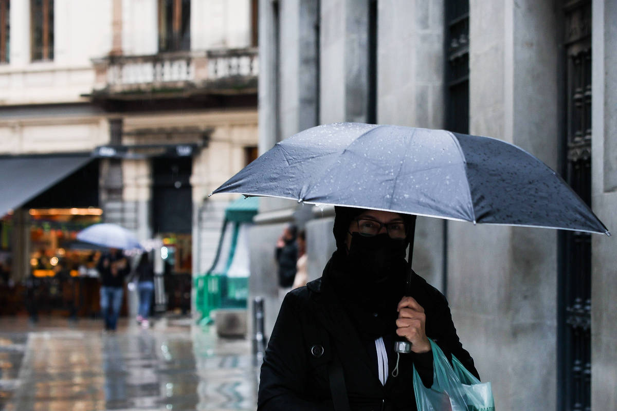 Pedestres com guarda-chuvas em rua molhada no centro de São Paulo