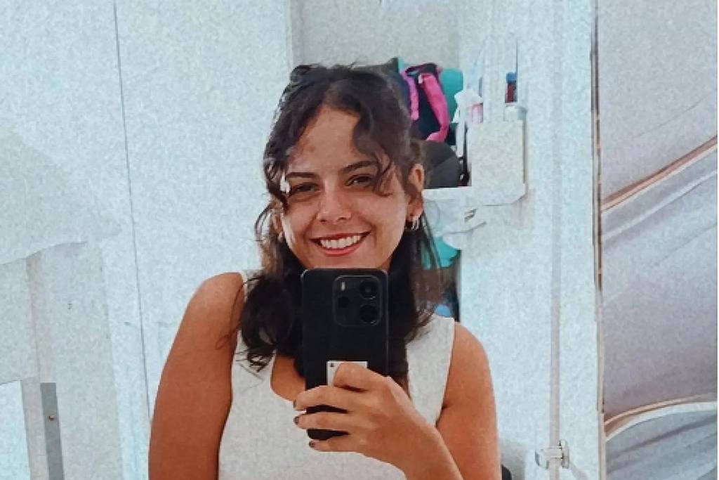 Giulia Silva de Araújo segura celular para tirar selfie em ambiente interno