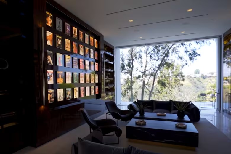 Sala de estar da mansão The One com parede de capas de revistas e janelas amplas