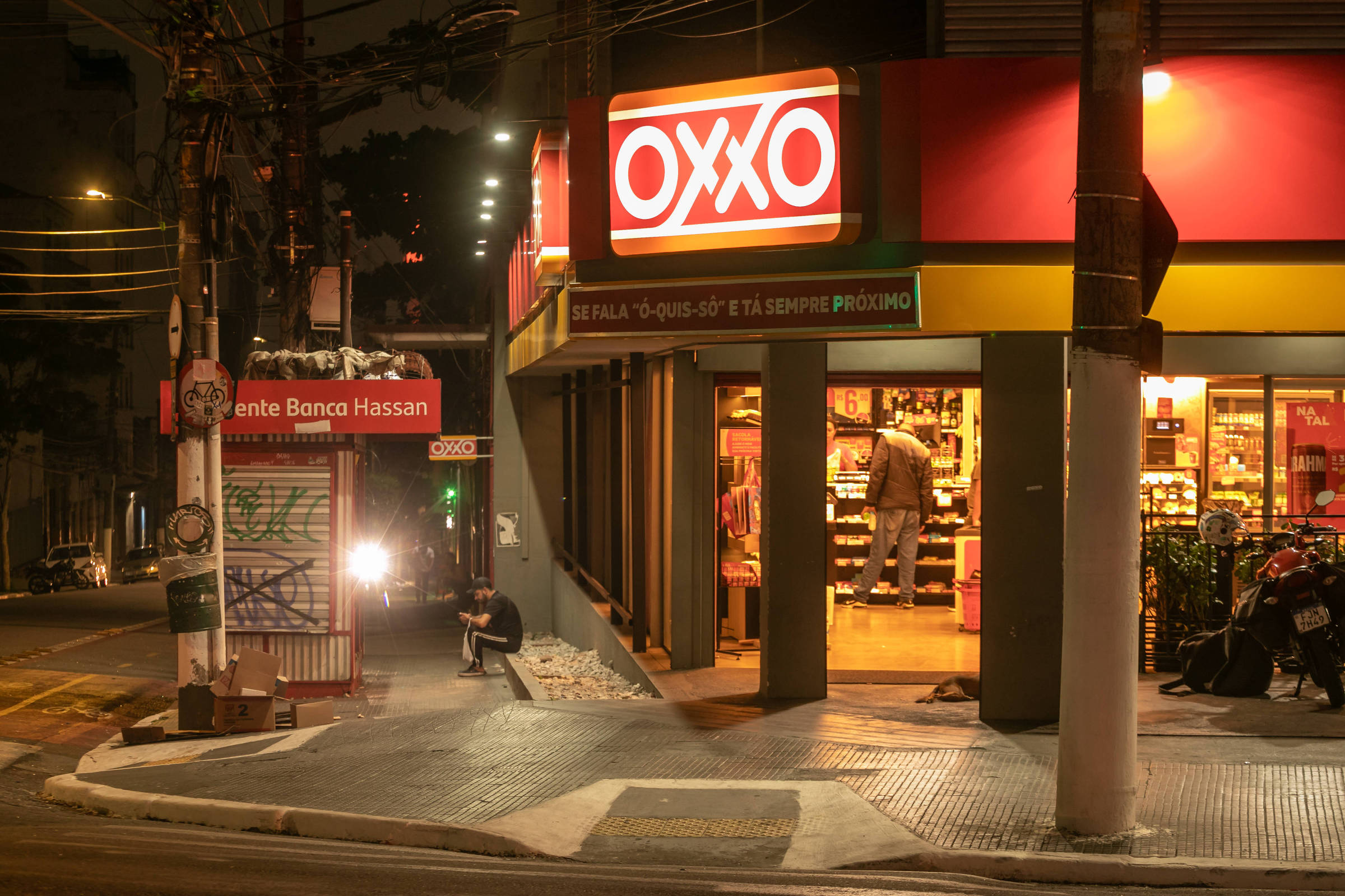 Loja Oxxo com fachada vermelha e amarela iluminada à noite