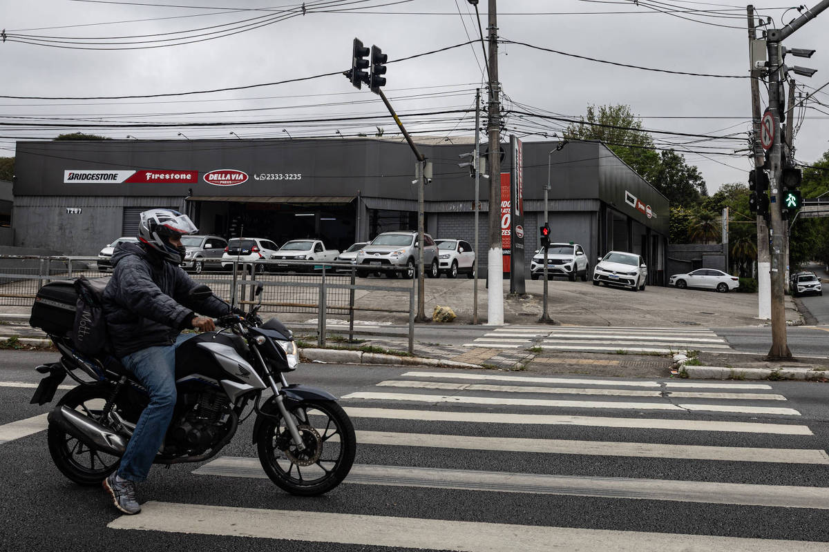 Motociclista cruza faixa de pedestres em avenida urbana