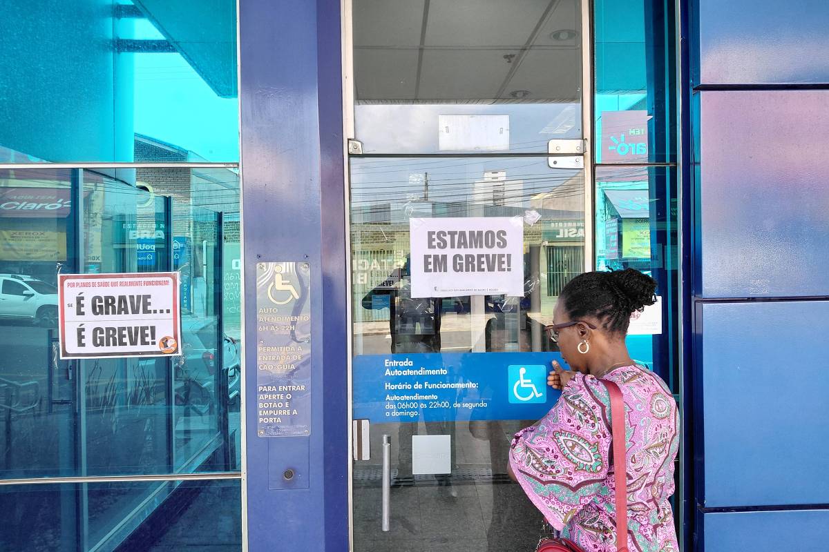 Mulher diante de agência da Caixa com cartazes de greve nas portas