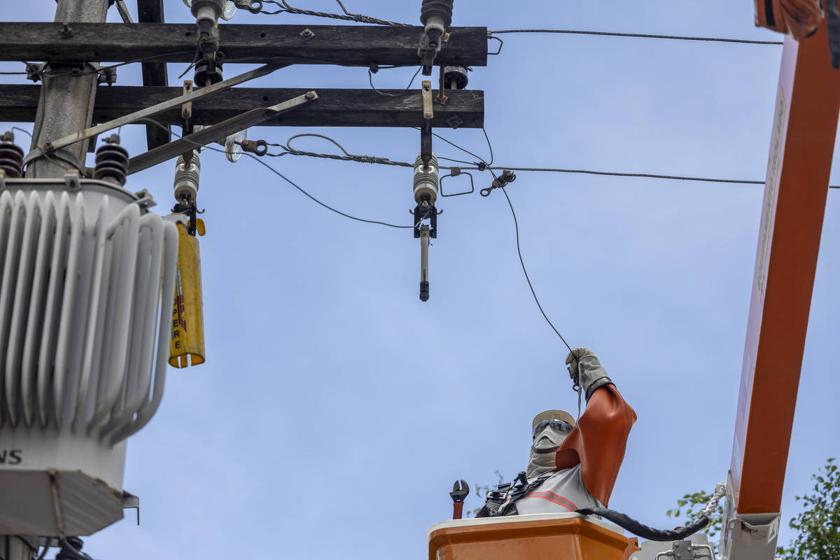 Técnico em cesta elevatória manuseia cabos em poste