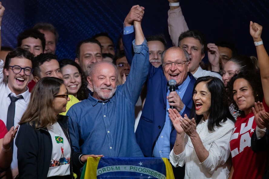 Lula e Geraldo Alckmin erguem os braços após a reeleição, cercados por apoiadores