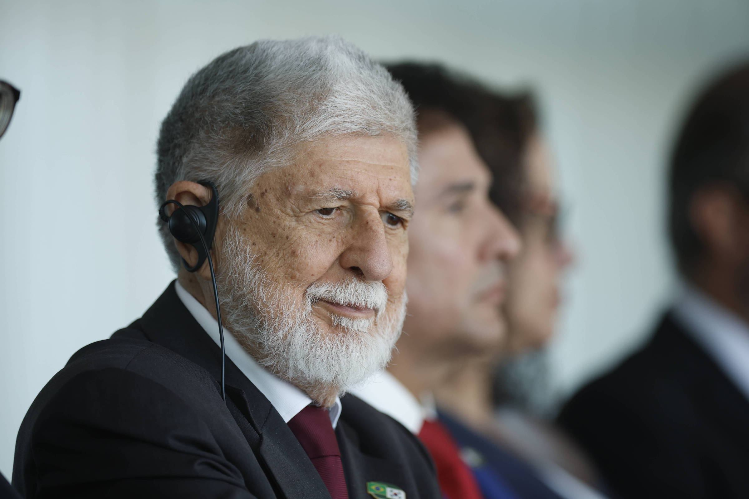 Celso Amorim de terno escuro e gravata vermelha usa fones de ouvido
