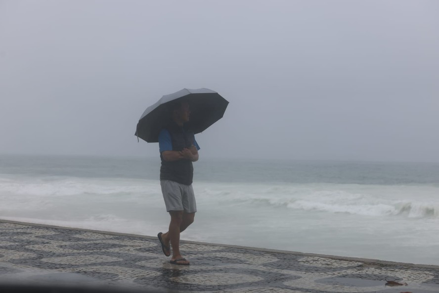 Homem se protege da chuva no calçadão da orla