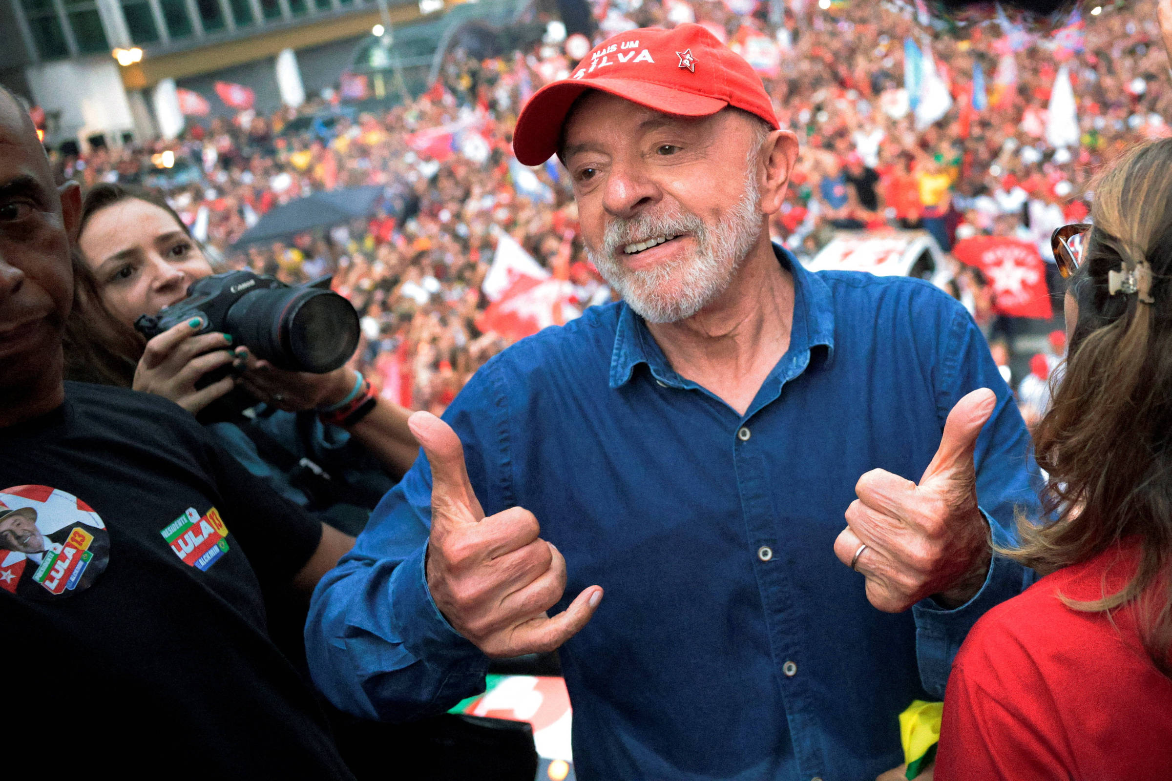 Lula de camisa azul e boné vermelho faz gesto diante de multidão