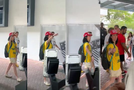 Eleitora de camisa amarela e boné faz gesto com o braço erguido em pátio de escola