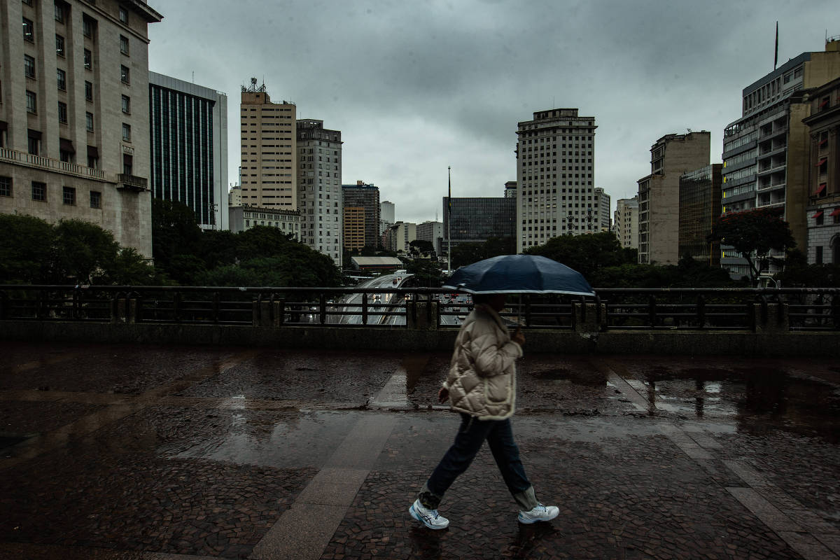 Mulher com guarda-chuva azul caminha sob chuva no centro de São Paulo