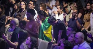 Pessoas em culto com mãos levantadas e homem envolto em bandeira do Brasil