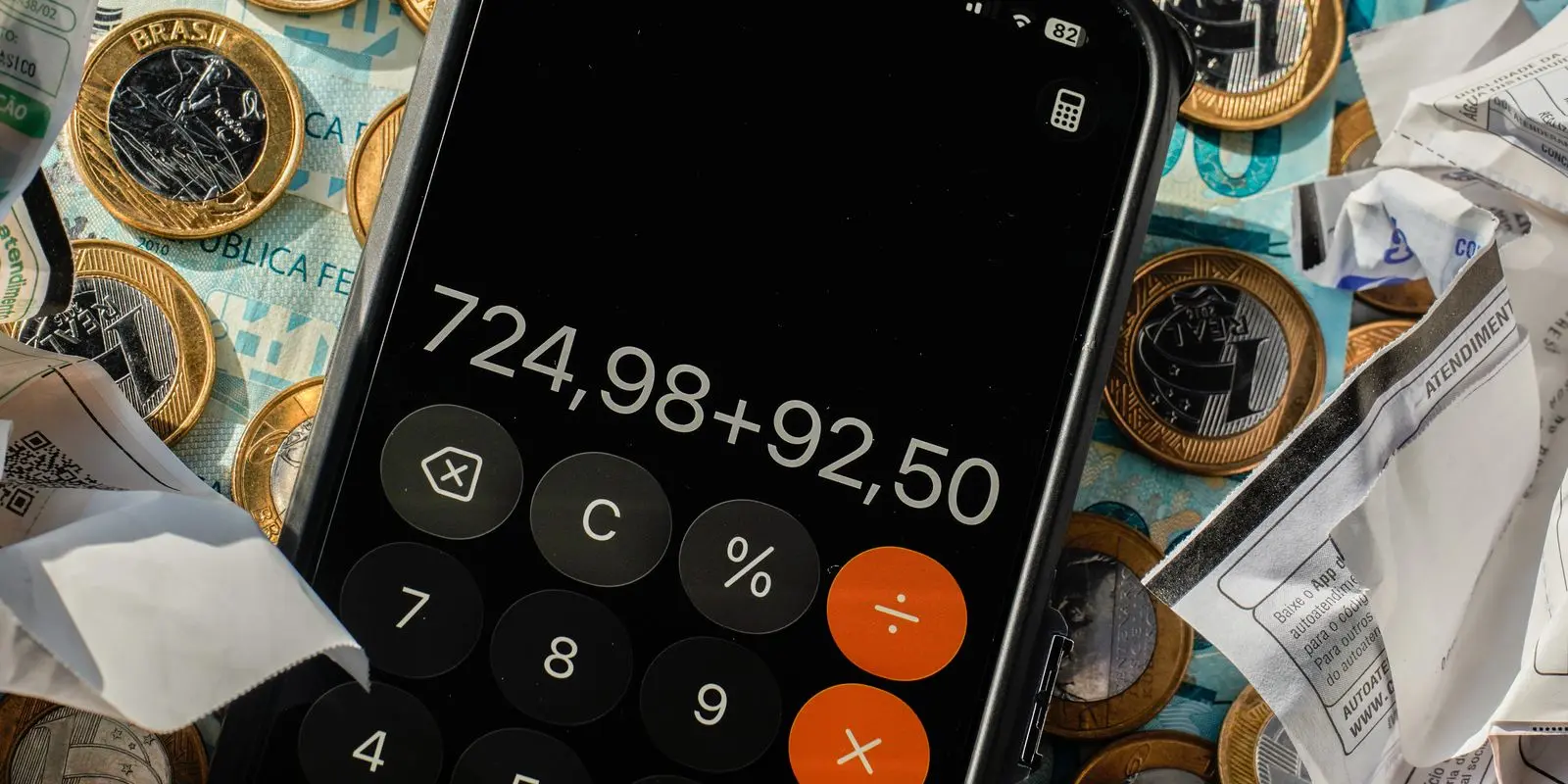 Calculadora em celular sobre cédulas e moedas de real