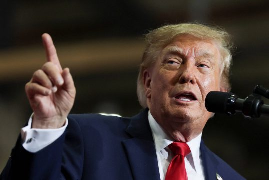 Donald Trump fala ao microfone e levanta o dedo indicador durante comício
