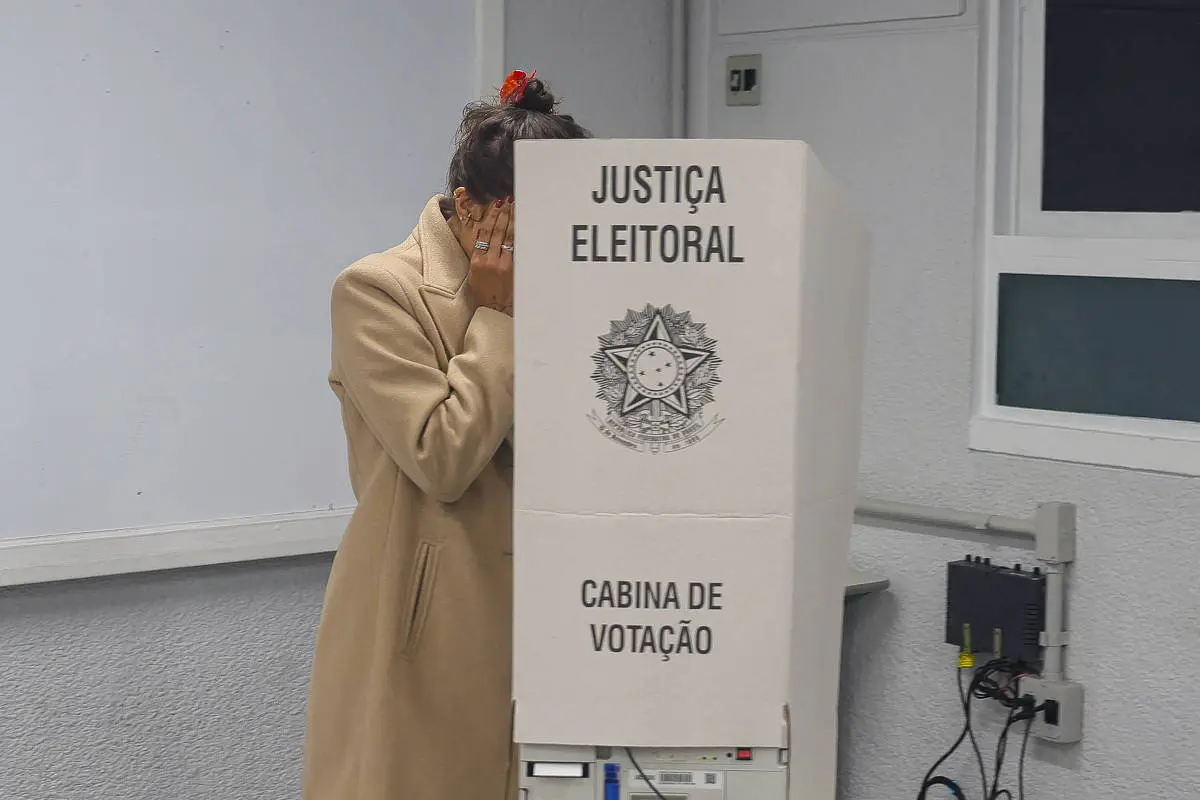 Eleitora de casaco bege vota em cabine eleitoral